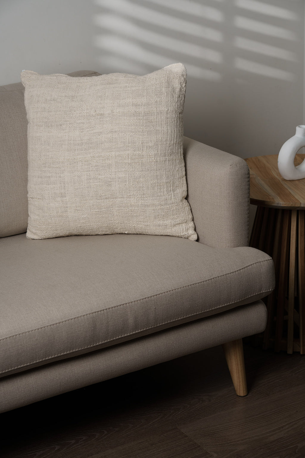 Beige pillow on a sofa with a wooden side table in the background