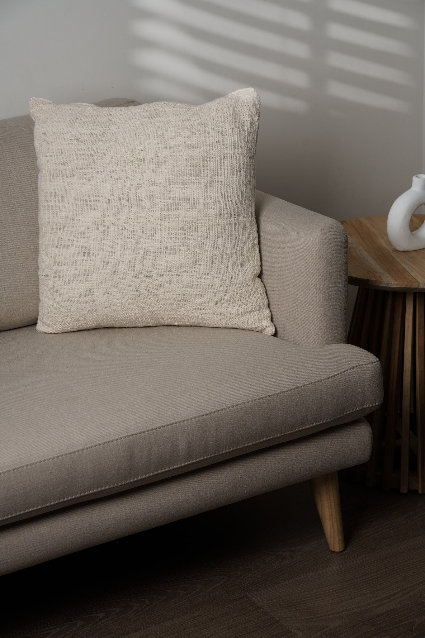 Beige pillow on a sofa with a wooden side table in the background